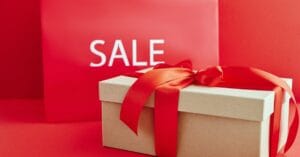 Gift box with red ribbon on red background with sale sign, perfect for retail promotions.